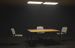 Image of an empty table surrounded by three chairs in a darkened room