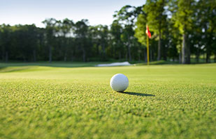 Close up image of a golf ball sitting on well-trimmed golf course grass with a flag off in the distance (Thinkstock)
