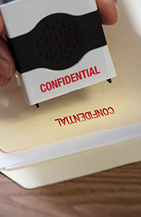 Image of a hand holding a pre-inked stamper above the word 'Confidential' stamped onto a file folder