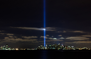 Image of the New York City skyline at night showing the beam of light ascending into the sky from the 9/11 memorial site