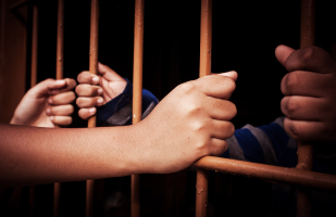 Image of hands on jail cell bars