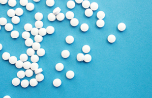 Iamge of dozens of small white pills scattered around on a sky-blue background