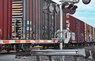 Several train cars passing a railroad crossing with the gate down and lights flashing.