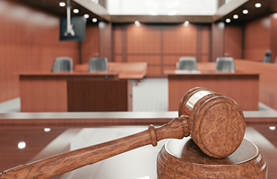 Close-up image of a wooden gavel sitting on a table in front of an empty courtroom