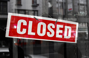 Image of a red sign with white lettering that says 'Closed' hanging in a window.