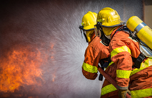 Image of two firefighters spraying water onto a fire.