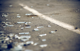 Close-up image of shards of broken glass on an asphalt parking lot.