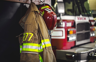 Image of a firefighters coat and helmet hanging on hooks in a firehouse.