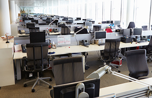 An open office space full of empty desks, chairs, and computers.