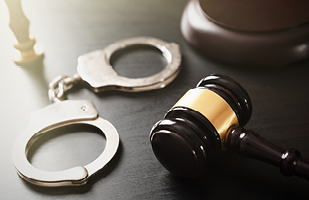 Image of a pair of handcuffs lying next to a wooden gavel.