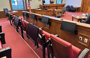 Image showing an empty jury box in a courtroom. Several monitors are mounted in front of jurors' seats.