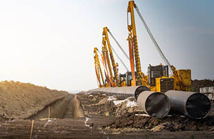 A long line of large, metal pipes lying on dirt.
