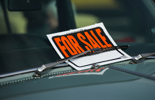 A 'For Sale' sign affixed to the windshied of a car using the wiper blade.
