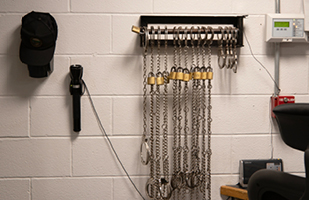 A white cinder block wall on which is hanging a rack of prisoner shackles.