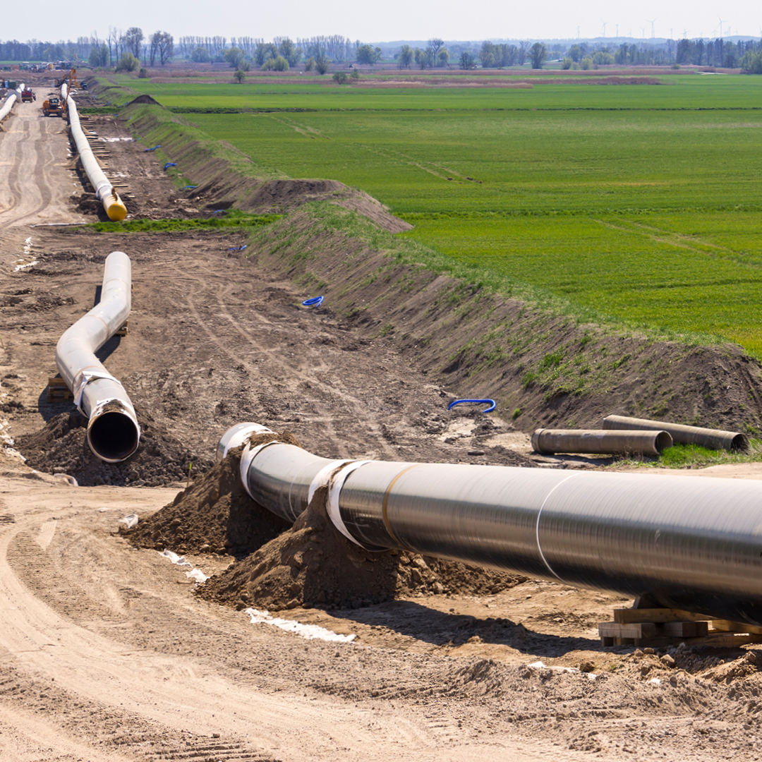 A long line of  large, metal pipes lying on dirt.