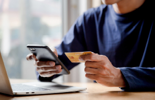A person holding a cellphone in one hand and a credit card in the other.