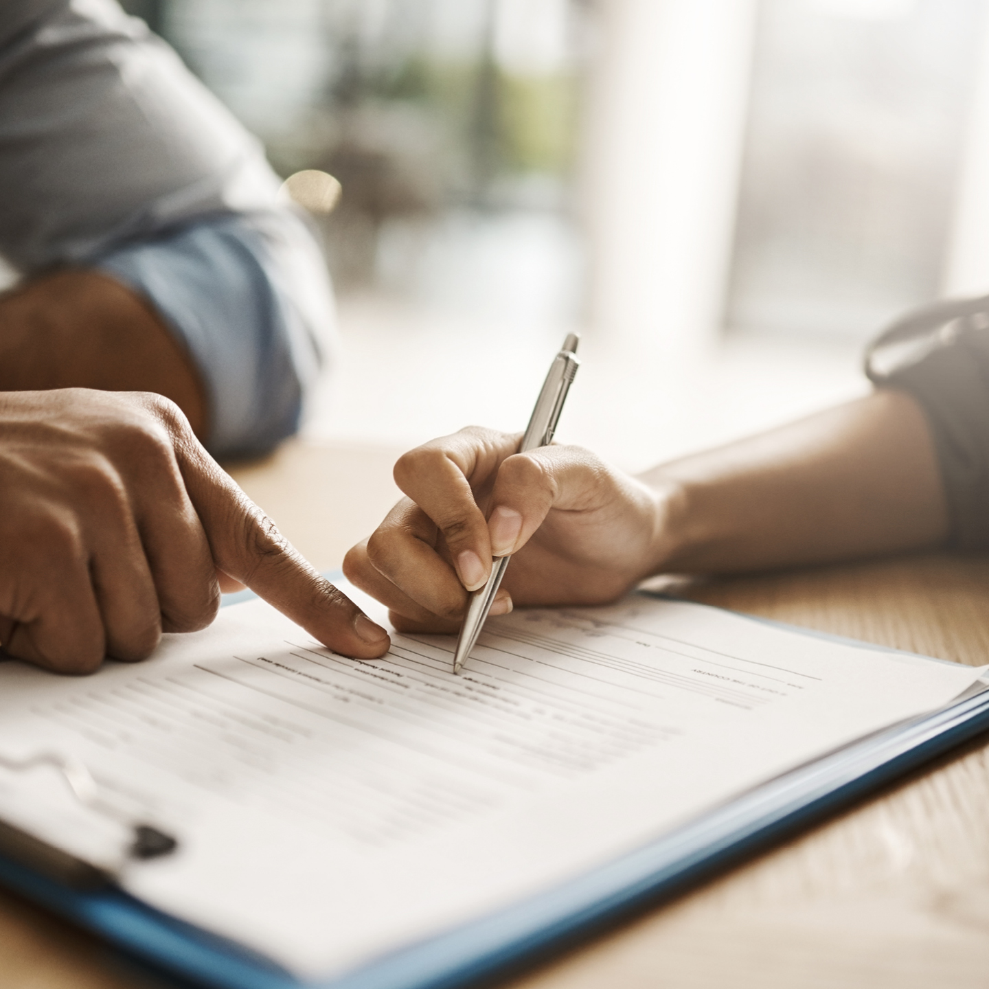 A person's hand holding a sleek silver pen, poised to sign a formal document resting on a blue clipboard.