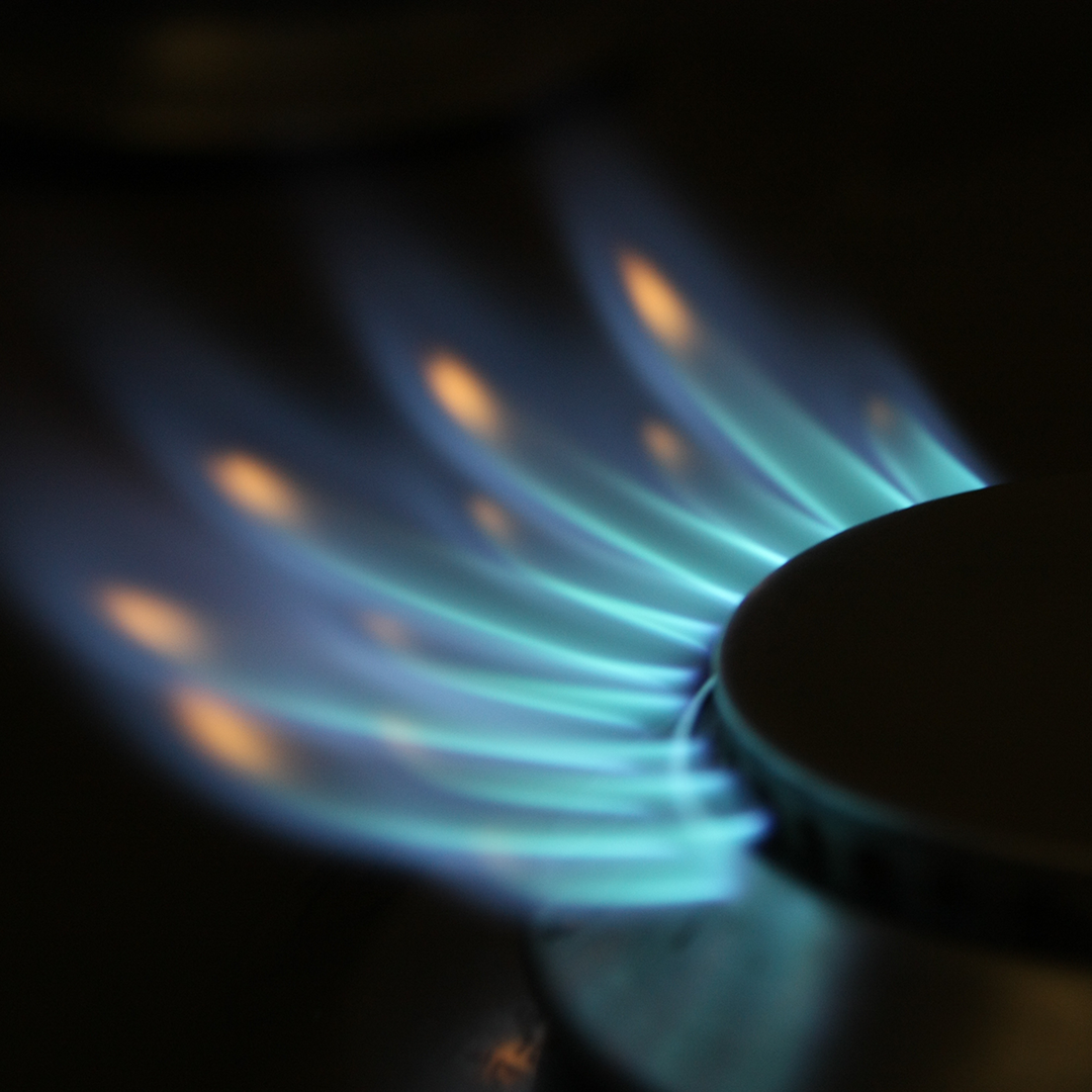 A close-up shot of a gas stove burner lit with bright blue and turquoise flames against a dark background.