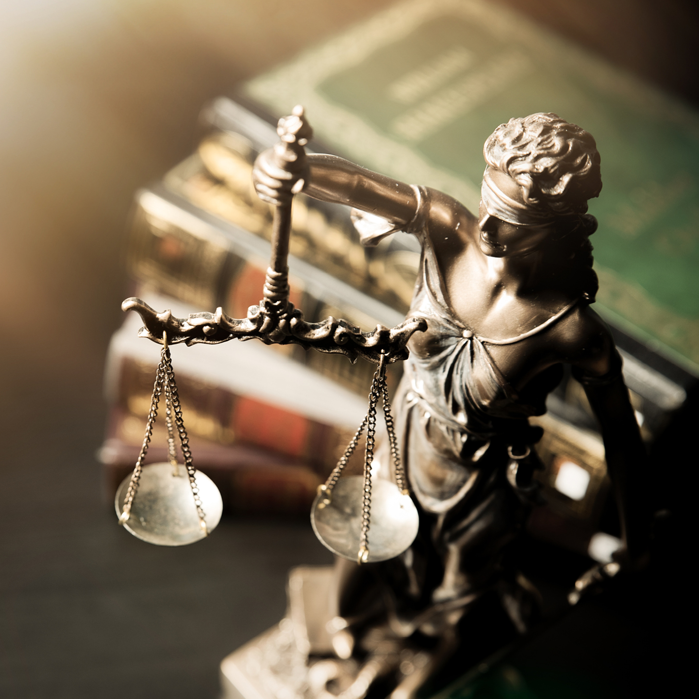 A bronze statue of Lady Justice next to a stack of vintage, leather-bound law books.