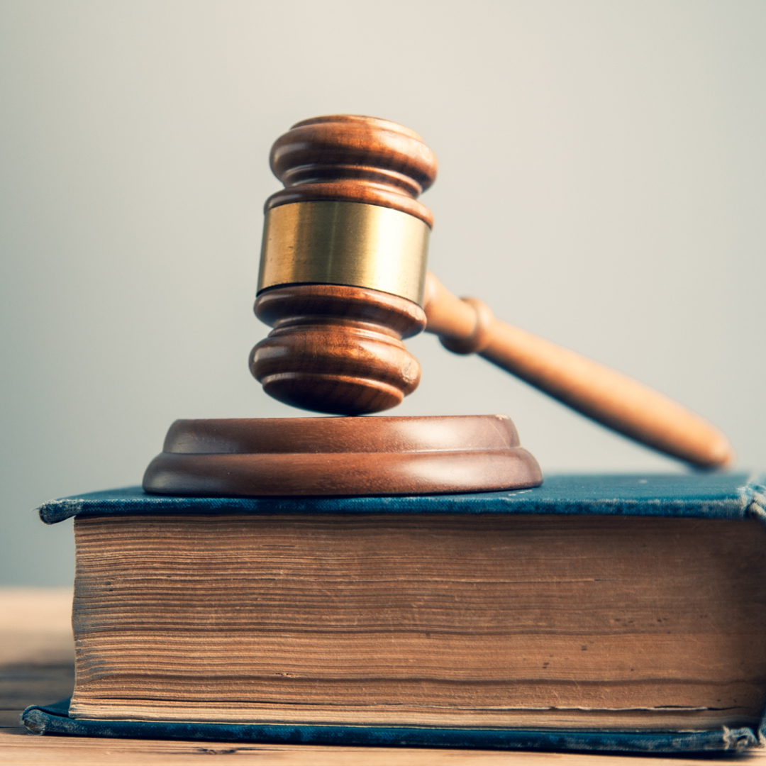 A wooden judge's gavel resting on a round sound block, which sits on top of a thick, worn blue law book with visible aged pages.