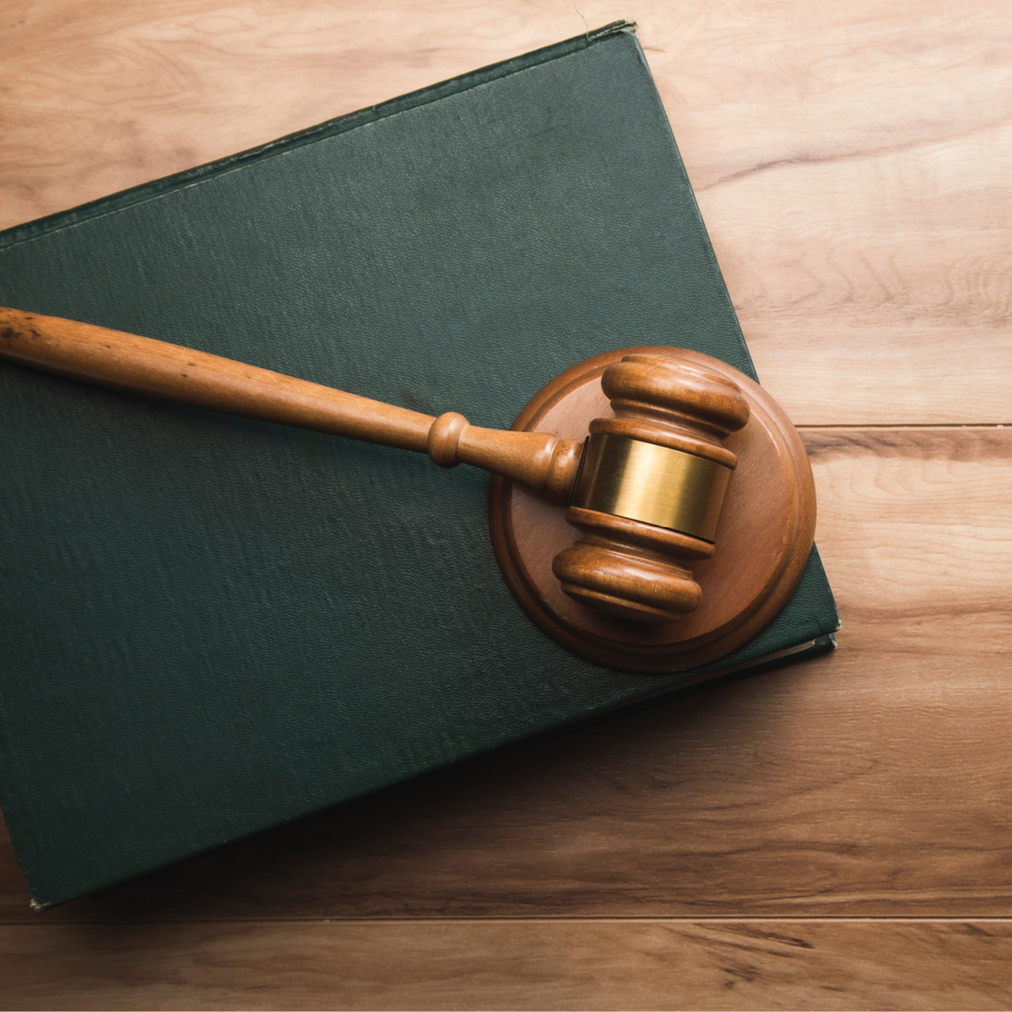 Wooden judge’s gavel resting on a sound block atop a closed law book on a wooden surface.