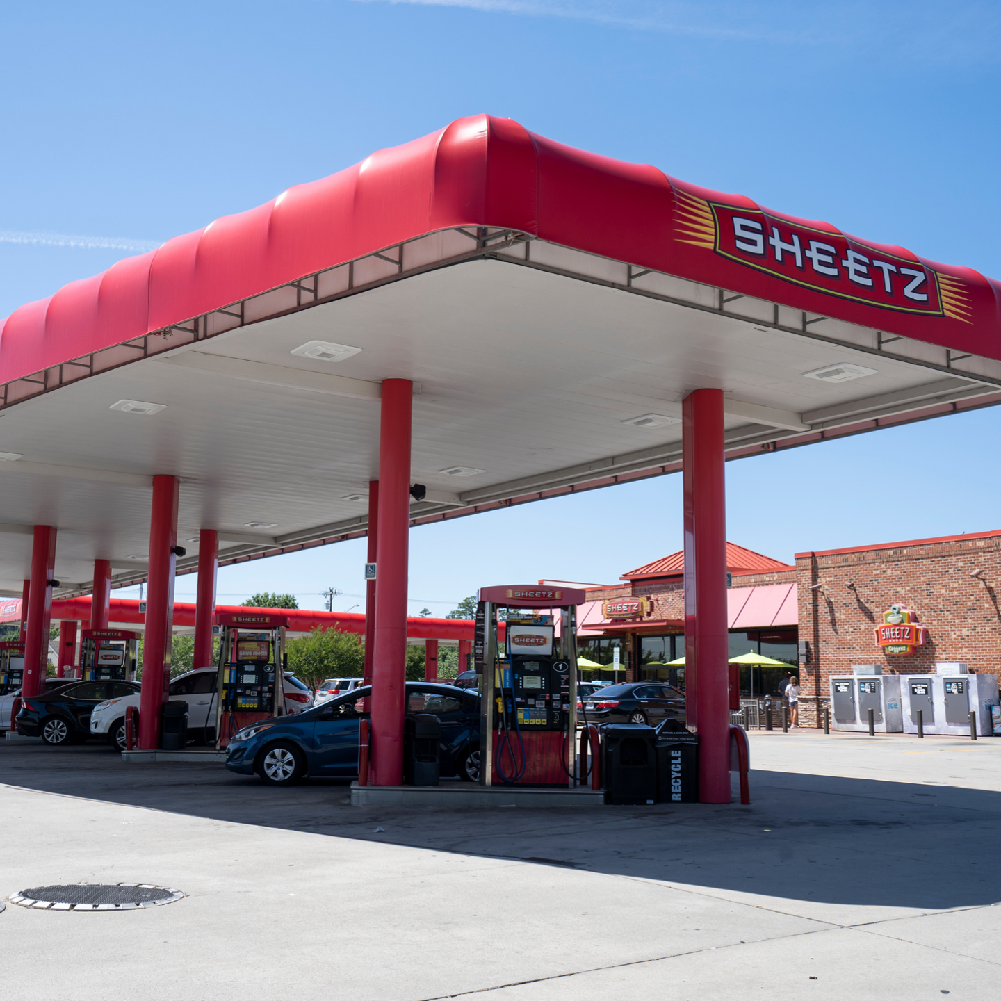 Sheetz gas station with red fuel pumps, parked cars, and a brick convenience store beneath a large red canopy.