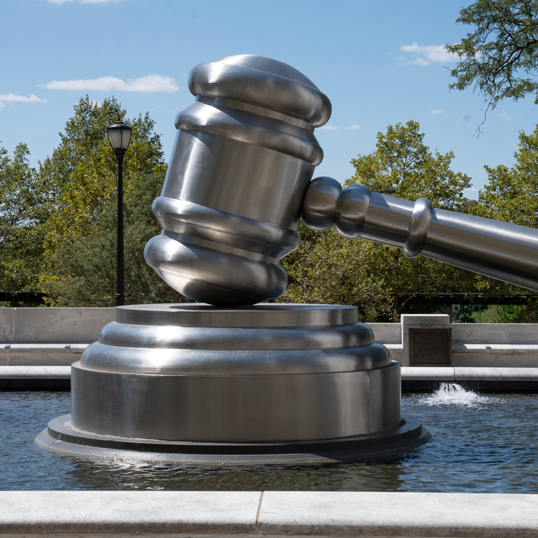 An oversized stainless steel sculpture of a judicial gavel and sound block, resting in the center of a shallow water fountain.