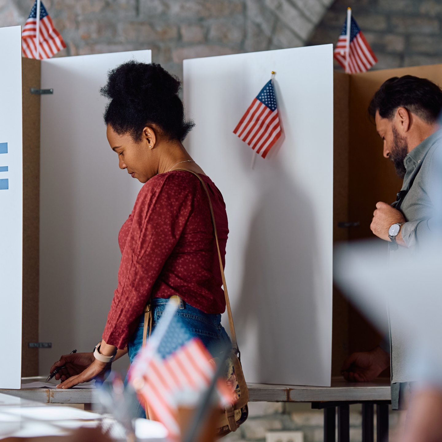 A side-profile view of a woman with her hair in a high bun casting her ballot inside a voting booth.