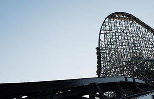 A large rounded metal track bends toward the ground from several hundreds of feet in the air with six carts carrying people in them.