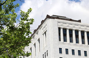 A white court building with trees, blue skies, and clouds in the background.