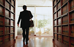 Image of a lawyer walking between a library stack of law books