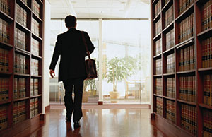 Image of a lawyer walking between a library stack of law books Image of a lawyer walking between a library stack of law books