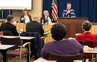 Image of a woman speaking at a podium to a room full of people