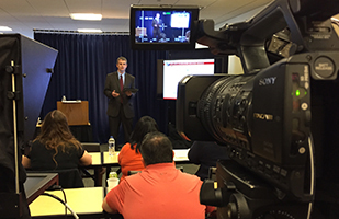 Image of a man speaking in front of a video camera Image of a man speaking in front of a video camera