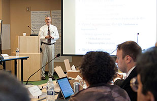 Image of a man standing next to a wooden podium addressing a roomful of people