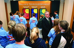Image of Visitor Education Center longtime volunteer Pete Miller speaking to a group of students in front of the Balance Your Government interactive display Image of Visitor Education Center longtime volunteer Pete Miller speaking to a group of students in front of the Balance Your Government interactive display
