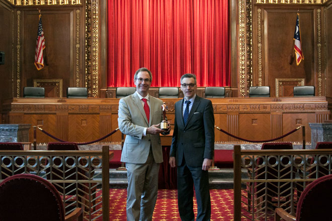 Image of Chris Davey and Dan Shellenbarger holding the Telly Award statue in the courtroom of the Thomas J. Moyer Ohio Judicial Center