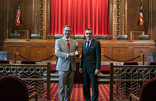 Image of Chris Davey and Dan Shellenbarger holding the Telly Award statue in the courtroom of the Thomas J. Moyer Ohio Judicial Center