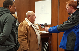 Photo of man in tan coat being interviewed by TV reporter Photo of man in tan coat being interviewed by TV reporter