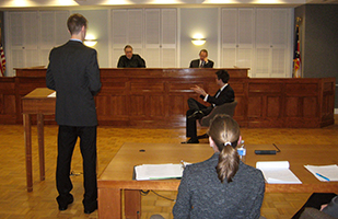 Image of high school students in a courtroom playing the parts of witnesses and attorneys in a mock trial