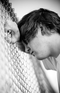 Image of a young man resting his head on his forearm, leaning against a chain link fence Image of a young man resting his head on his forearm, leaning against a chain link fence