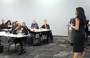 A woman stands addressing a roomful of people