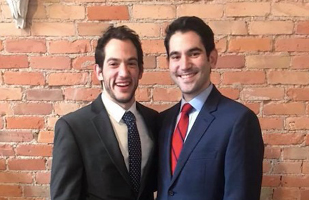 Image of two men wearing suits standing in front of a brick wall