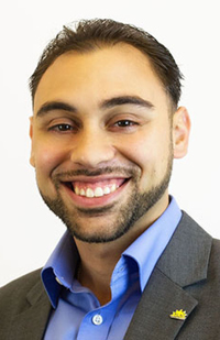 Image of a man smiling, wearing a blue dress shirt and grey suit coat