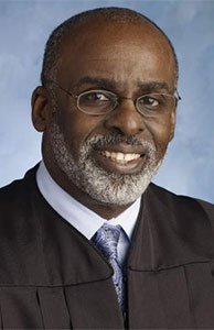 Image is headshot of former Judge Ronald Adrine in his black judicial robe