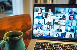 Image of a laptop with the screen showing multiple people in separate screen  blocks appearing to participate in a webinar, with a coffee mug in the foreground