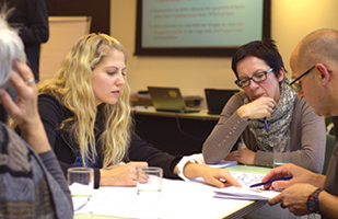 Image of two women and a man sitting at a table. The women appear to be assisting the man with paperwork.