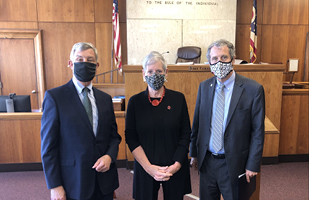 Image of two men and a woman wearing facial coverings standing in a courtroom