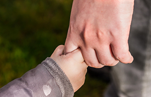 Close-up image of a man's hand holding a child's hand