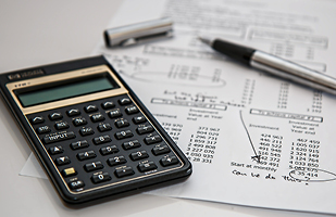 Image of a claculator and pen laying on top of a paper listing expenses